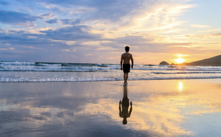 Mann am Strand blickt bei Sonnenuntergang aufs Meer.